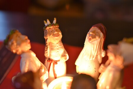 Fyra små figurer i keramik står runt ett ljus, troligen juldekorationer.