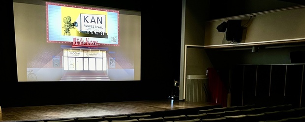 En tom biosalong med rader av stolar och en filmduk som visar en affisch för en filmfestival.