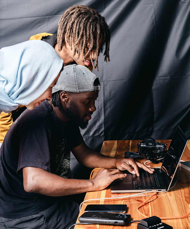 Tre personer samarbetar vid en bärbar dator på ett träbord med teknikprylar.