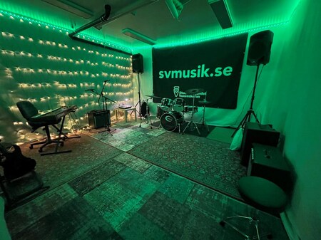 Musikstudio med trumset, keyboard, förstärkare och gröna LED-lampor längs väggarna.