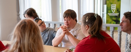 En grupp personer sitter runt ett bord och samtalar i ett ljust rum.