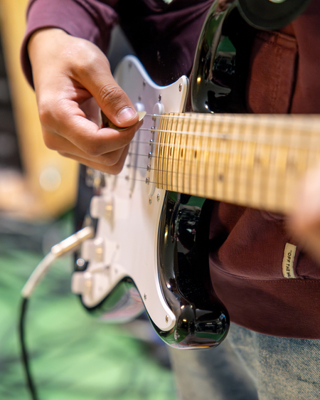 En person spelar elgitarr, närbild på händer och gitarrens strängar.