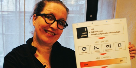 Kvinna med glasögon håller upp en informationsskylt om sångteknik och ler mot kameran.