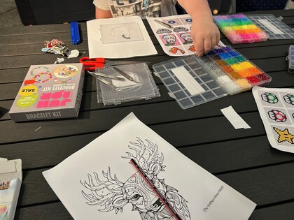 Ett bord med pärlplattor, färgglada pärlor, armbandssats, sax och en teckning av en hjort.