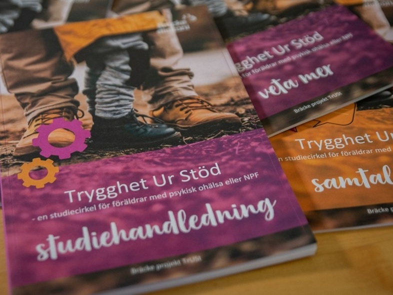 Flera broschyrer med titeln 'Trygghet Ur Stöd' ligger utspridda på ett bord.