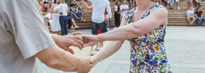 Två personer dansar tillsammans utomhus, med publik sittande i bakgrunden.