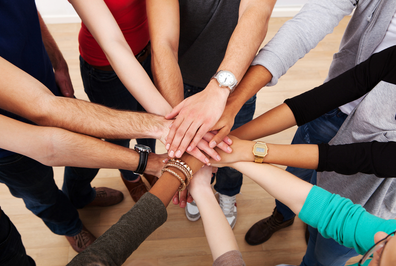Flera personer står i en cirkel och lägger sina händer ovanpå varandra i mitten.