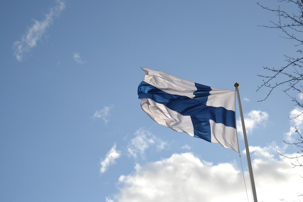 Finlands flagga vajar mot en blå himmel med några moln.