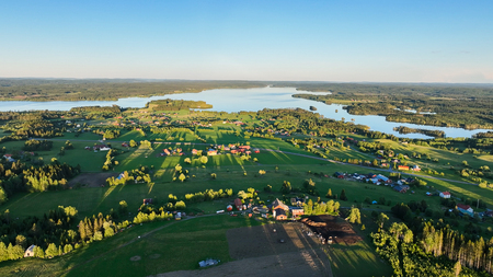 Landskapsvy över gröna fält, gårdar och sjöar under klarblå himmel.