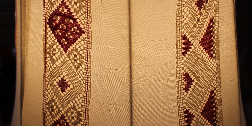 Närbild av en lampskärm med broderade och virkade mönster i beige och vinrött.