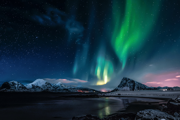 Norrsken lyser upp natthimlen över snötäckta berg och en frusen kust.