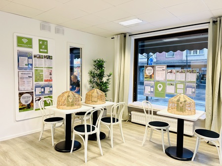 Ljust café med vita stolar, små bord och stora fönster mot gatan. Informationsblad på väggarna.