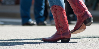 Person i blå jeans och röda cowboyboots dansar utomhus på asfalt.
