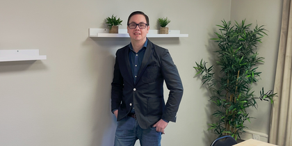 En person står vid väggen i ett mötesrum med bord, stolar, växter och hyllor med krukväxter.