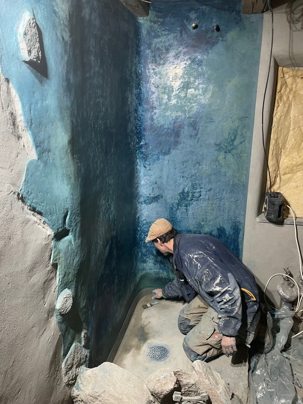 En person målar eller behandlar en duschvägg med blå nyanser i ett rum under renovering.