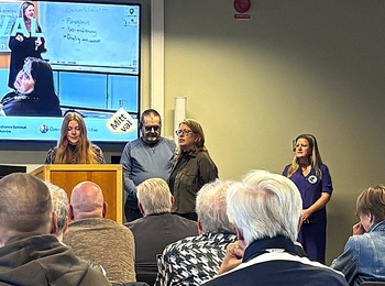 Möte eller presentation i konferensrum med flera personer, en talare vid podiet och publik som lyssnar.