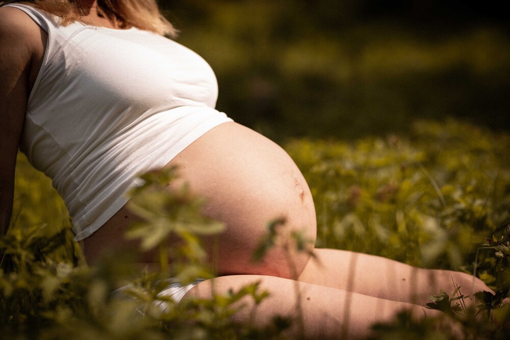 En gravid kvinna sitter utomhus i gräset med fokus på hennes mage.