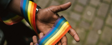 Två händer håller ett regnbågsfärgat band, symbol för HBTQ+-rörelsen.
