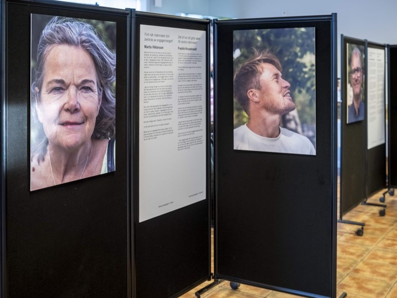 Utställning med porträttfotografier och texter på svarta skärmar i ett rum med klinkergolv.