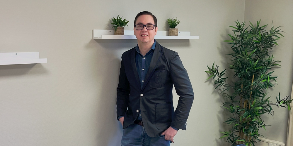 En person står vid väggen i ett mötesrum med bord, stolar, växter och hyllor med krukväxter.