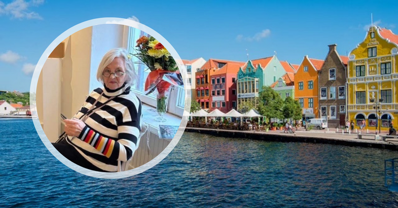 Kvinna i randig tröja sitter vid fönster med blommor, bakgrund med färgglada hus vid vattnet.