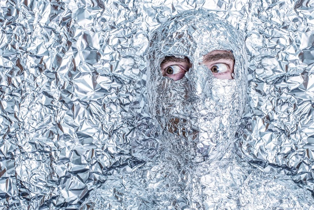 En person är täckt av skrynklig aluminiumfolie mot en bakgrund av mer aluminiumfolie.