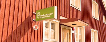 Röd träbyggnad med vita fönster och en grön skylt med texten 'Studieförbundet Vuxenskolan'.