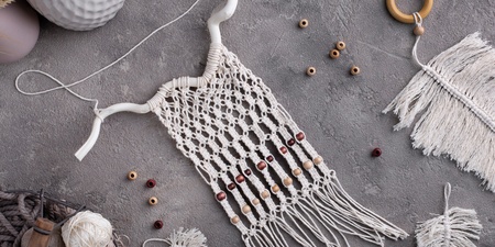 Makraméprojekt med garn, träpärlor och tillbehör på ett grått bord.
