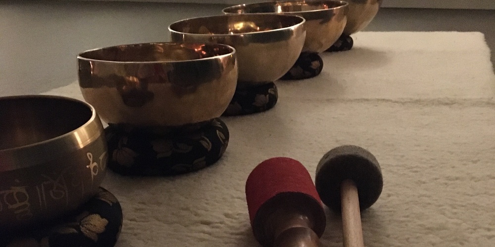 Fem tibetanska klangskålar står på rad på en matta med två klubbor framför dem i ett dämpat rum.