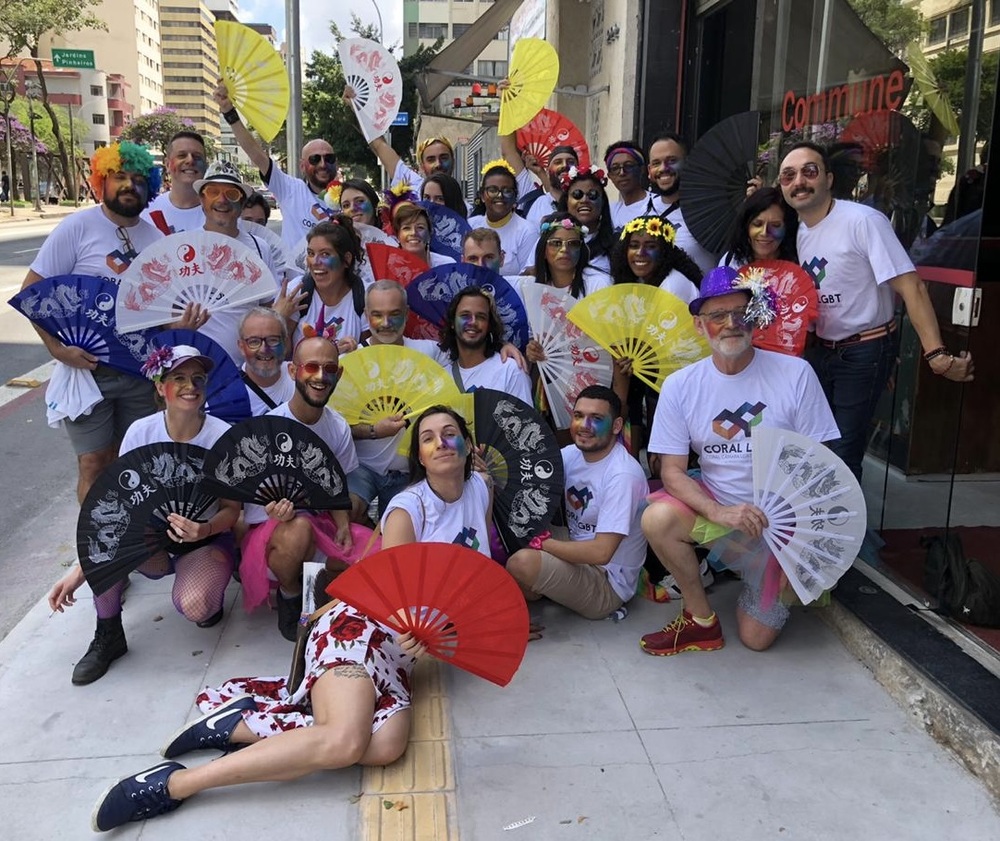 En grupp människor poserar utomhus med färgglada solfjädrar och t-shirts med regnbågsmotiv.