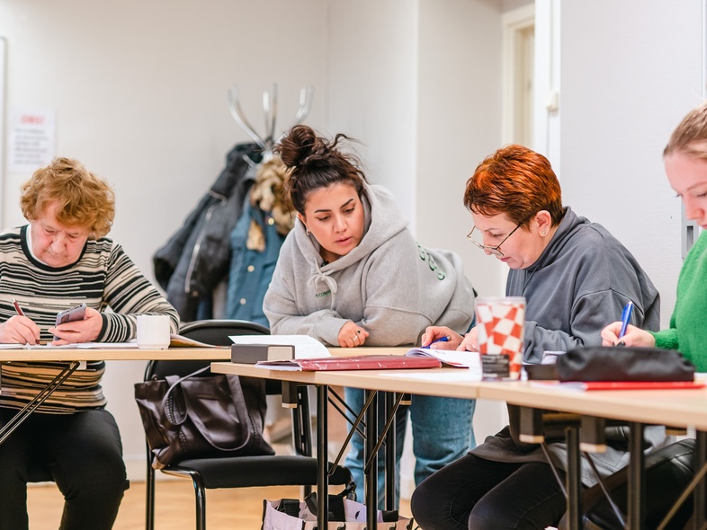 Fyra personer sitter vid ett bord och arbetar tillsammans med papper och pennor i ett klassrum.
