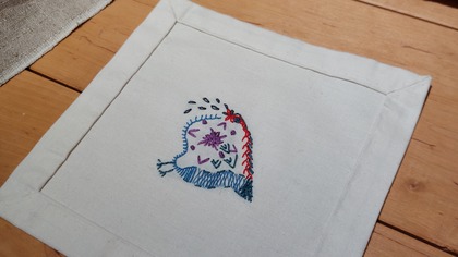 En tygbit med broderat mönster i olika färger ligger på ett trägolv.