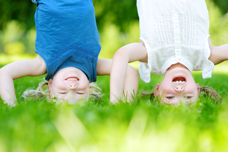 Två barn gör kullerbyttor på gräsmatta och ler mot kameran, upp och ner.