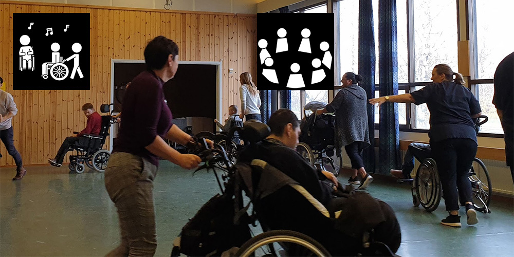 Personer i rullstol och personal deltar i en aktivitet i en ljus sal med träväggar och stora fönster.