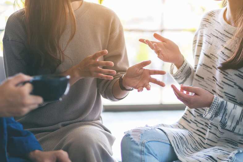 Tre personer sitter och samtalar och gestikulerar med händerna.