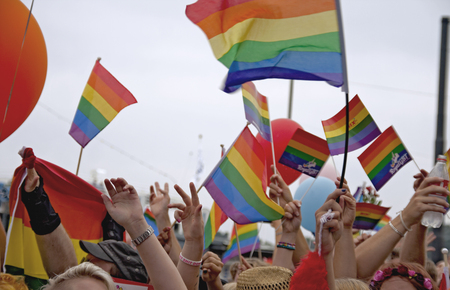 Människor viftar med regnbågsflaggor på en prideparad, händer och flaggor syns i färgglad folkmassa.
