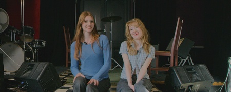 Två personer sitter på en scen i ett rum med musikinstrument och högtalare.