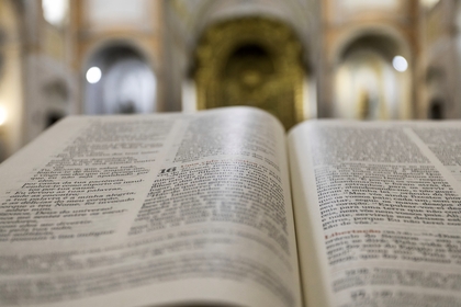En uppslagen bok, troligen en bibel, ligger i fokus i en kyrka med suddig bakgrund.