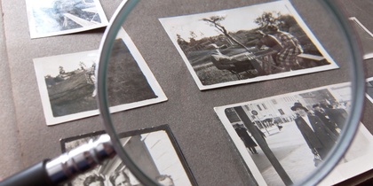 Ett fotoalbum med svartvita fotografier granskas med ett förstoringsglas.