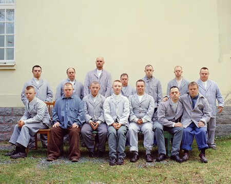 Gruppfoto av män i liknande kläder utomhus framför en ljus vägg, ansikten är suddade.