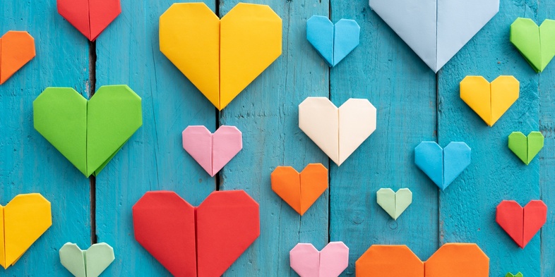 Flera färgglada origamihjärtan i olika storlekar på en blå träbakgrund.
