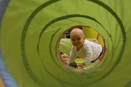 Ett litet barn kryper genom en grön lektunnel och tittar mot kameran.