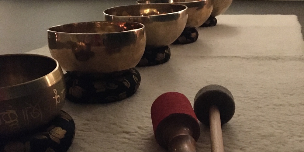 Fem tibetanska klangskålar står på rad på en matta med två klubbor framför dem i ett dämpat rum.
