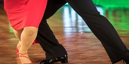 Två personer dansar tillsammans på ett dansgolv, endast deras ben och fötter syns.