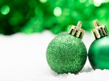 Två gröna julgranskulor står på konstsnö med suddig grön bakgrund.