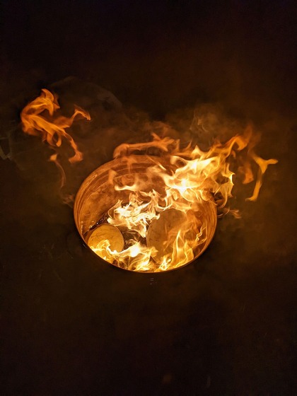 En eld brinner i en tunna i mörkret, med starka orangea lågor och rök.