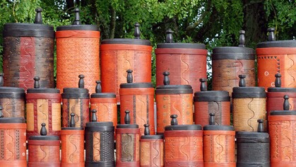 Flera färgglada, mönstrade trälådor med lock staplade utomhus framför gröna träd.