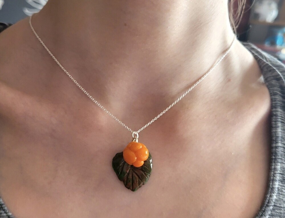 Närbild av en hals med ett halsband med ett orange bär och ett grönt blad som hänge.