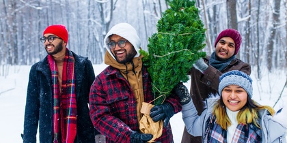 Fyra glada personer bär en julgran i en snöig skog, klädda i vinterkläder.