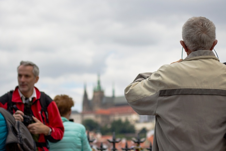 Flera personer står utomhus, några fotograferar, med en stadssilhuett och slott i bakgrunden.